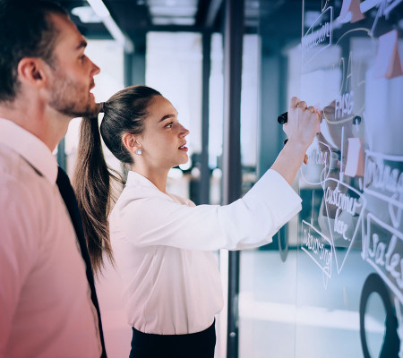 Zwei Personen stehen in einer Büro-Atmosphäre an einem Vision-Board und arbeiten aktiv an einer Prozessplanung. Die Simba ERP Software unterstützt Sie beim Aufbau transparenter Kommunikationsprozesse und dem Ausbau stabiler Kundenbeziehungen. 