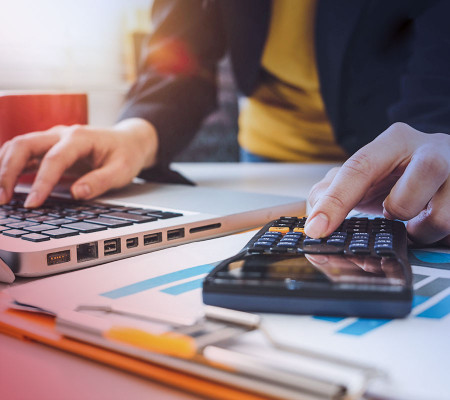 Das Bild zeigt eine Person, die gleichzeitig auf einem Laptop und einem Taschenrechner tippt. Die Person sitzt an einem Schreibtisch und trägt ein blaues Oberteil. Auf dem Schreibtisch befinden sich außerdem ein Ausdruck mit Diagrammen. Die Simba Buchhaltungssoftware sorgt durch die direkte Verknüpfung der Module Finanzbuchführung, Zahlungsverkehr, Bankkontierung/Banking in Verbindung mit der digitalen Belegerfassung für die termingenaue und automatisierte Abwicklung von Überweisungen und Lastsc
