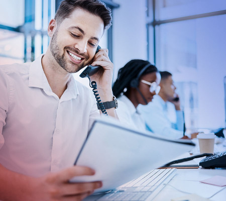 Ein freundlich schauender Mann richtet seinen Blick auf den das Dokument in seiner linken Hand. In seiner rechten Hand hält er ein Telefon. Im Hintergrund sieht man weitere Call-Center Mitarbeiter. Die automatisierten Prozesse der Simba Software entlasten Sie beispielsweise bei der Verwaltung immer wiederkehrender Rechnungen, z.B. Mitgliedsbeiträge, Speditionsbeiträge oder Lieferantenbestellungen. Automatisiert versendet die Simba ERP-Software erstellten Dokumente automatisiert im PDF-Format per