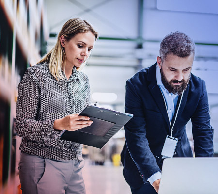 Das Bild zeigt zwei Personen in einer Arbeitssituation. Eine Frau hält ein Klemmbrett in der Hand, ein Mann ist über seinen geöffneten Laptop gebeugt. Es handelt sich hierbei um Vertriebsmitarbeiter. Mit der Simba ERP-Software erhalten Anwender jederzeit aussagekräftige Daten über Ihre Lagerbestände und ausstehende Lieferungen – egal, ob für Webshops oder im stationären Handel.