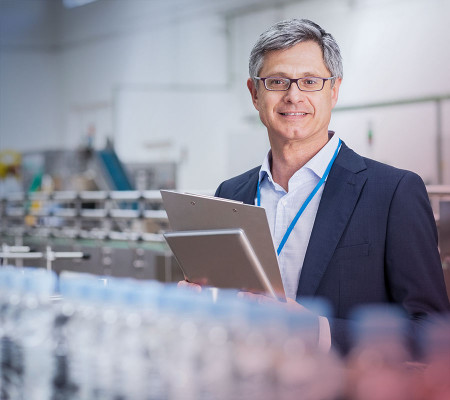Ein im Anzug gekleideter Mann steht mit einem Anzug in der Produktionshalle eines Industrieunternehmens